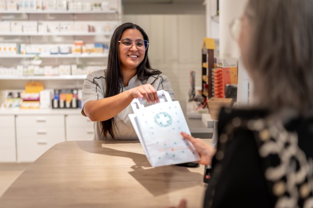 Pharmacist handing a bagged prescription to a customer at the pharmacy counter