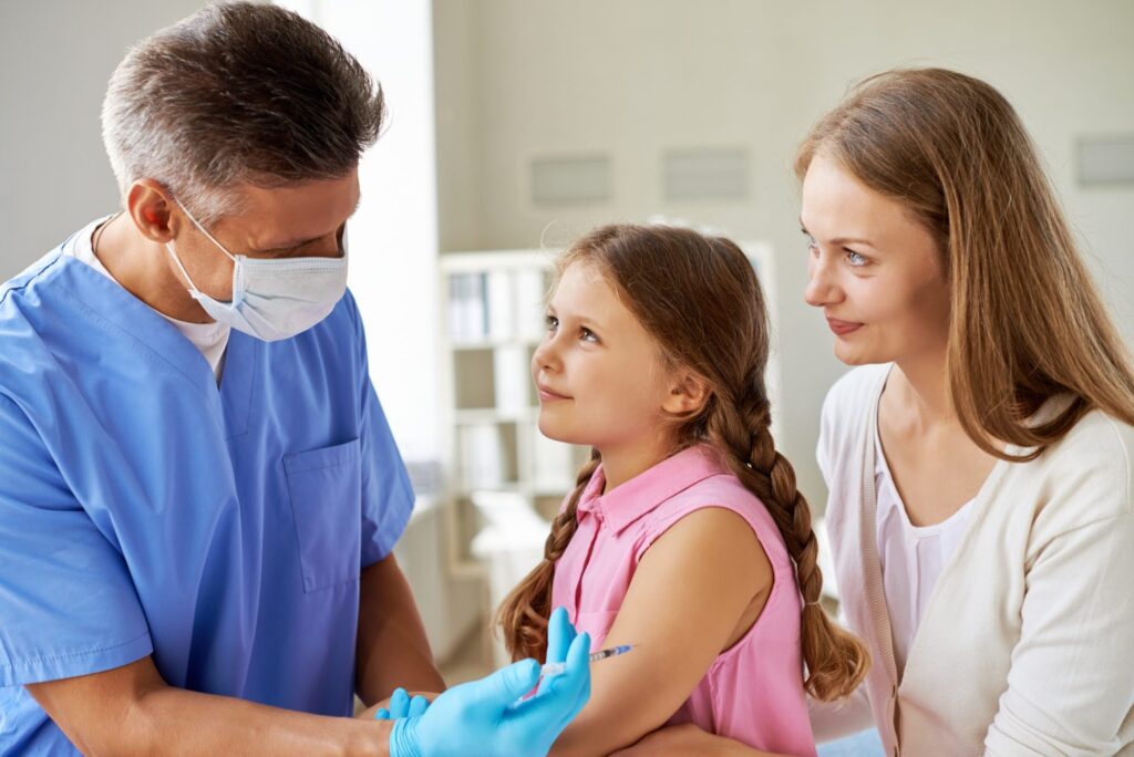 Pharmacist administering a vaccine to a young patient while her mother watches